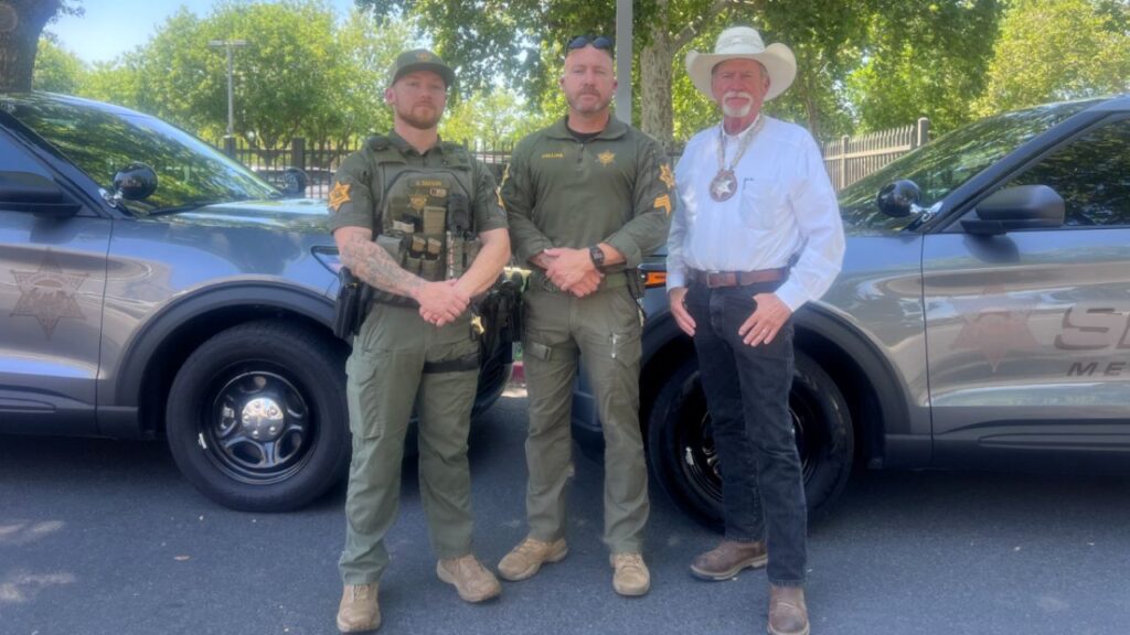 Image of Merced County Sheriff's deputies standing with Sheriff Vern Warnke in front of two gray patrol SUVs