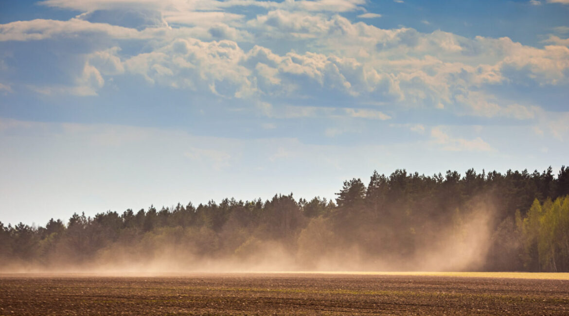Image of a dust storm on fallowed land below a blue sky and clouds