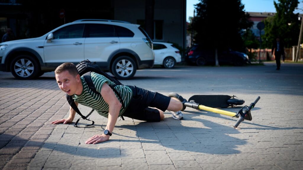 Image of a man who has fallen off of a motorized scooter and is sprawled on cement,