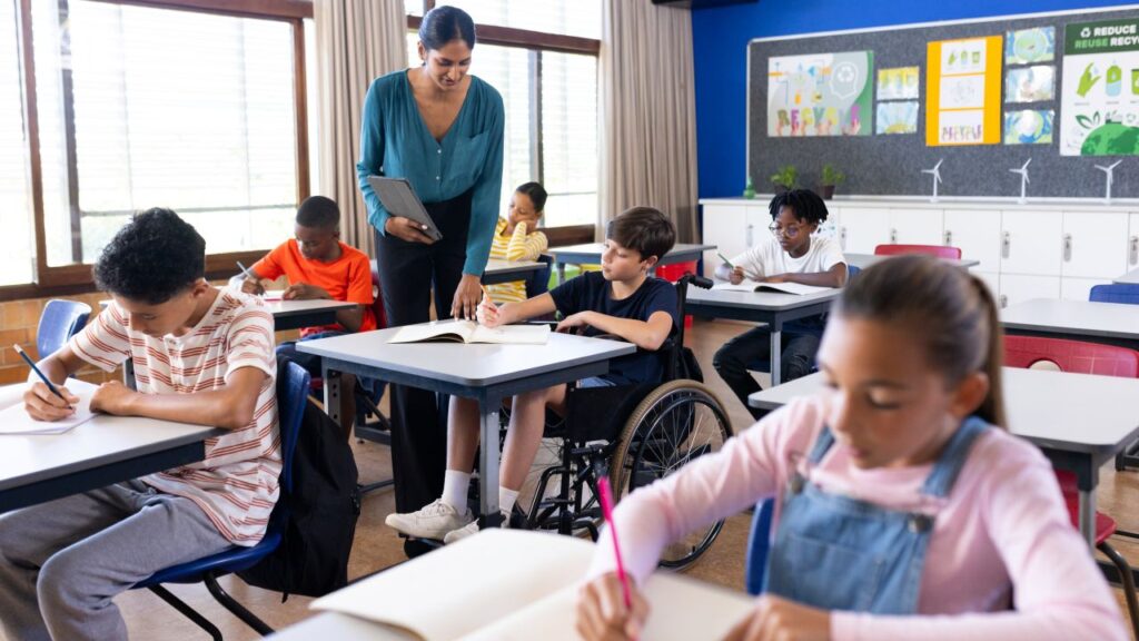 Image of a tall female teacher dressed in blue assisting students in a diverse California classroom