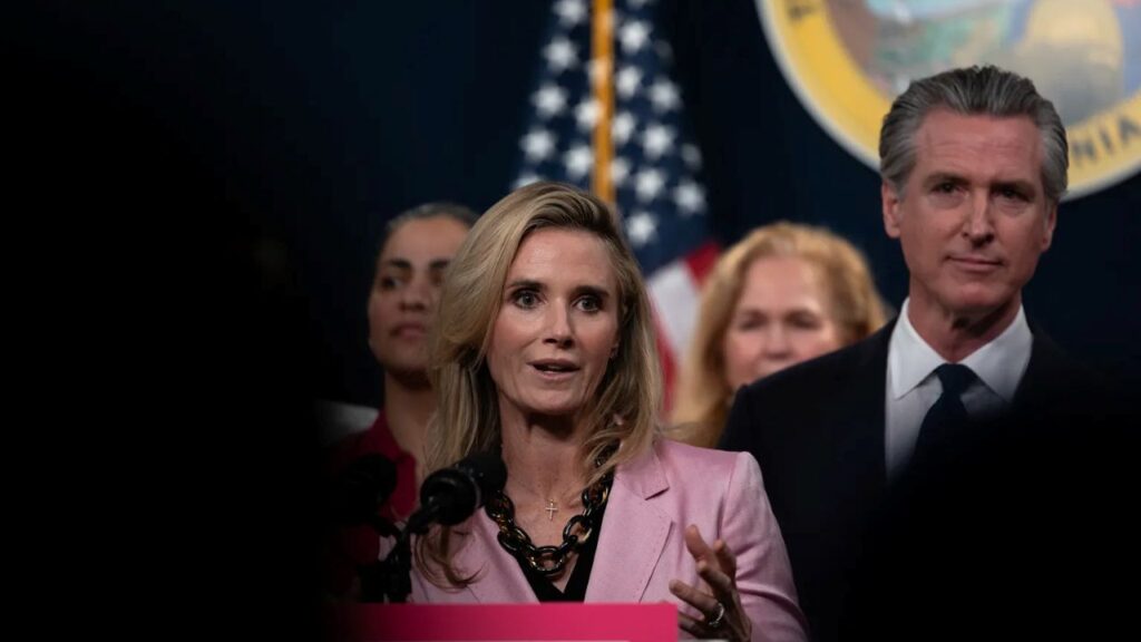 Image of a well-dressed woman and man standing at a podium with the American Flag and Seal of California in the background