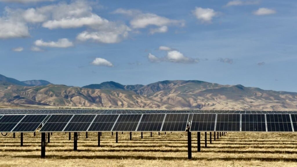 Image of a southern San Joaquin Valley solar farm against a foothills backdrop on a sunny day with clouds above