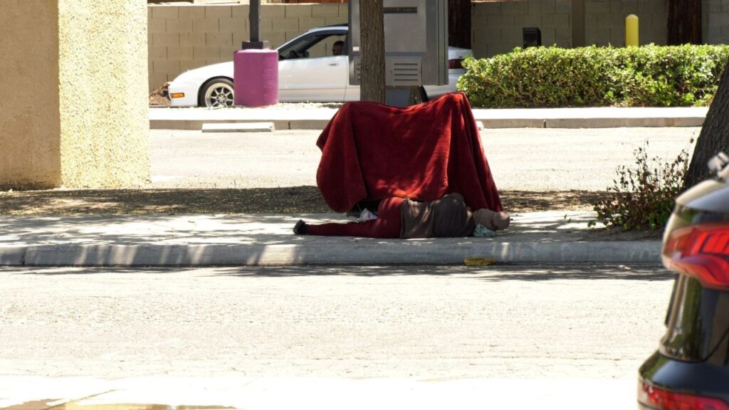 Picture of a homeless man wrapped in a red blanket sitting on a sidewalk