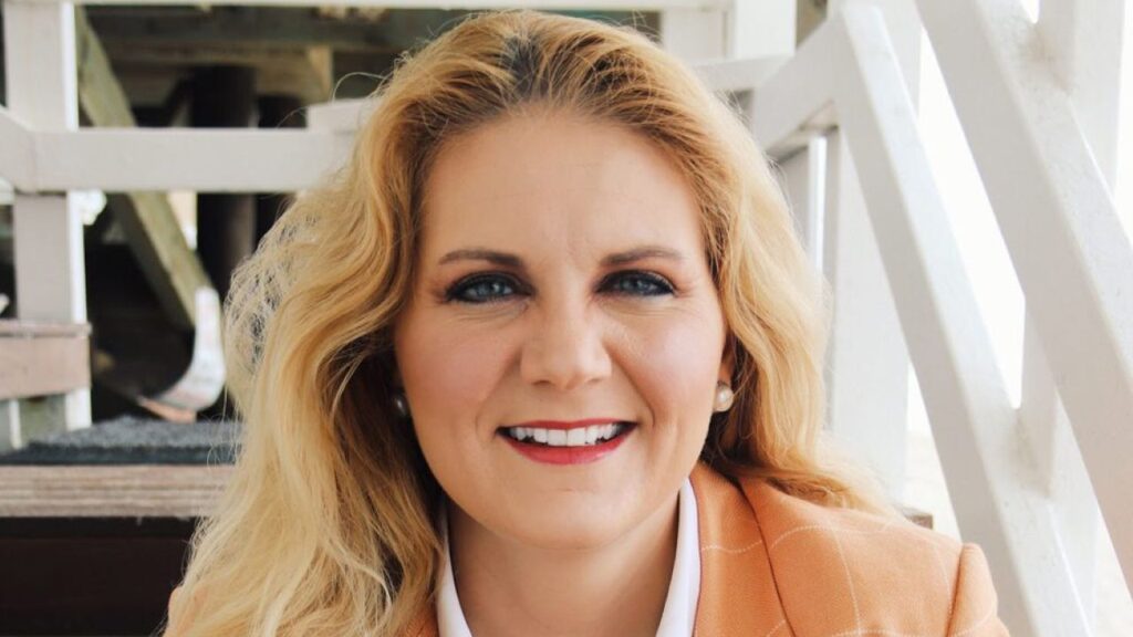 Environmental portrait of Aubrey Bettencourt sitting on stairs. She's wearing an orange blazer and a white open collar shirt