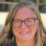 Portrait of Susan Phillips in casual clothing. She has blonde shoulder-length hair and is wearing glasses