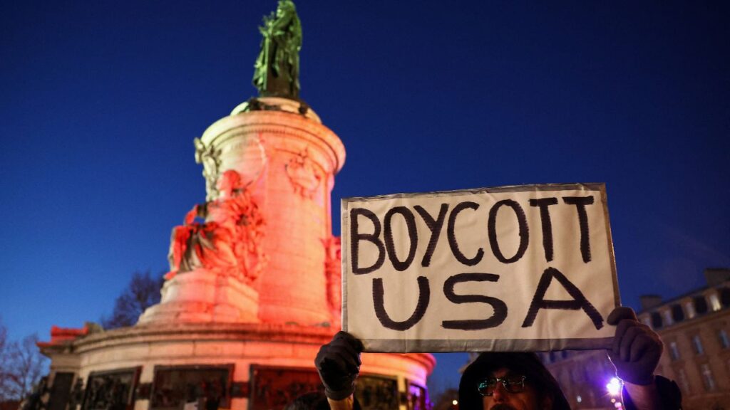 A man holds up 'Boycott USA' sign, as people demonstrate to oppose U.S. actions in Venezuela at a protest, after U.S. President Donald Trump said the U.S. has struck Venezuela and captured its President Nicolas Maduro, in Paris, France, January 3, 2026. REUTERS/Abdul Saboor