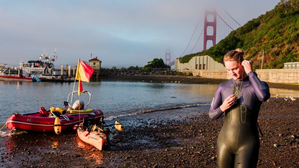 Image of a woman in a wet suit on a beach at San Francisco Bay with a red inflatable boat and a white kayak in the background