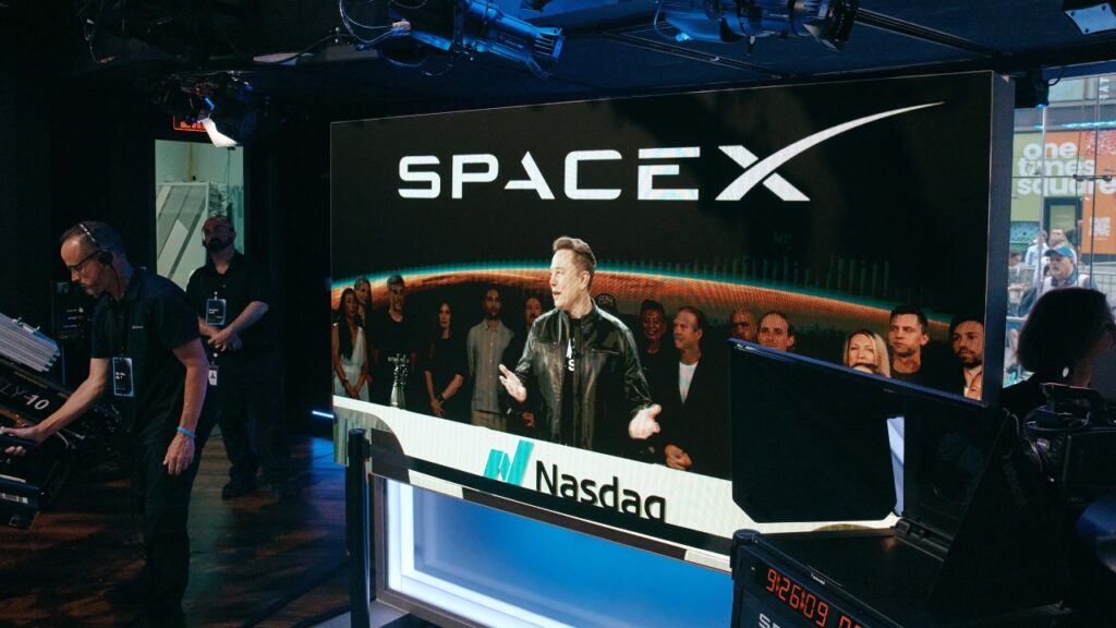 Elon Musk is visible on a video feed from Starbase, the Texas headquarters of SpaceX, at the Nasdaq stock exchange in New York on Friday morning, June 12, 2026. Musk became the world’s first trillionaire on June 11, 2026, as shares of his rocket company SpaceX began trading on the stock market at $150, up 11 percent from their initial public offering price. (Andres Kudacki/The New York Times)