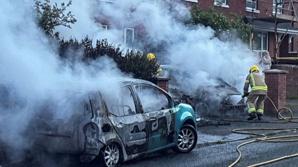 Firefighters work to extinguish a fire in three cars parked on the street at Tigers Bay, during a protest after a knife attack on June 8 left a man seriously injured and prompted police to declare a critical incident, in Belfast, Northern Ireland, June 9, 2026. (Reuters/Isabel Infantes)