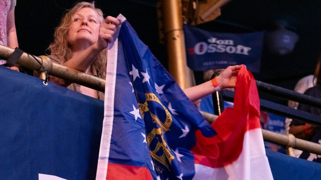A female supporter of Sen. Jon Ossoff unfurls a Georgia state flag at a campaign rally