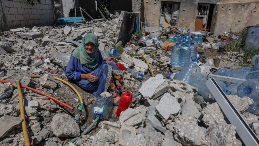 Khadija Amara, whom local residents said had not left her home, fills a jerrycan with water as she sits among the rubble of a house, which was damaged by an Israeli strike, in Qlaileh in the Tyre district, southern Lebanon, June 19, 2026. REUTERS/Zohra Bensemra