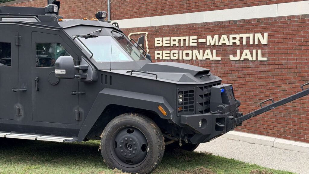 Image of an armored vehicle facing right near the red brick wall of a regional jail