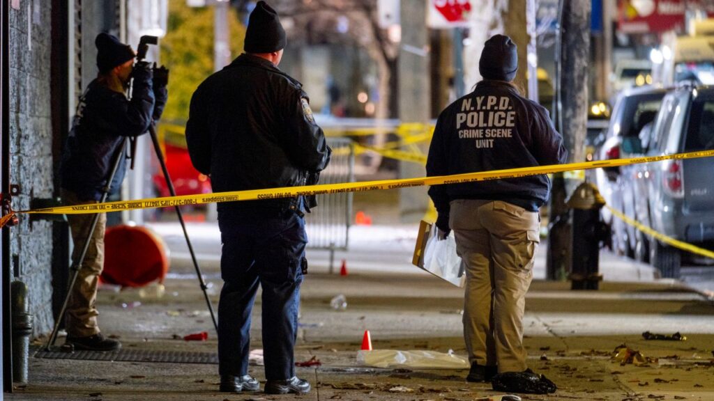 Image of the backs of police officers at a crime scene cordoned off with yellow tape