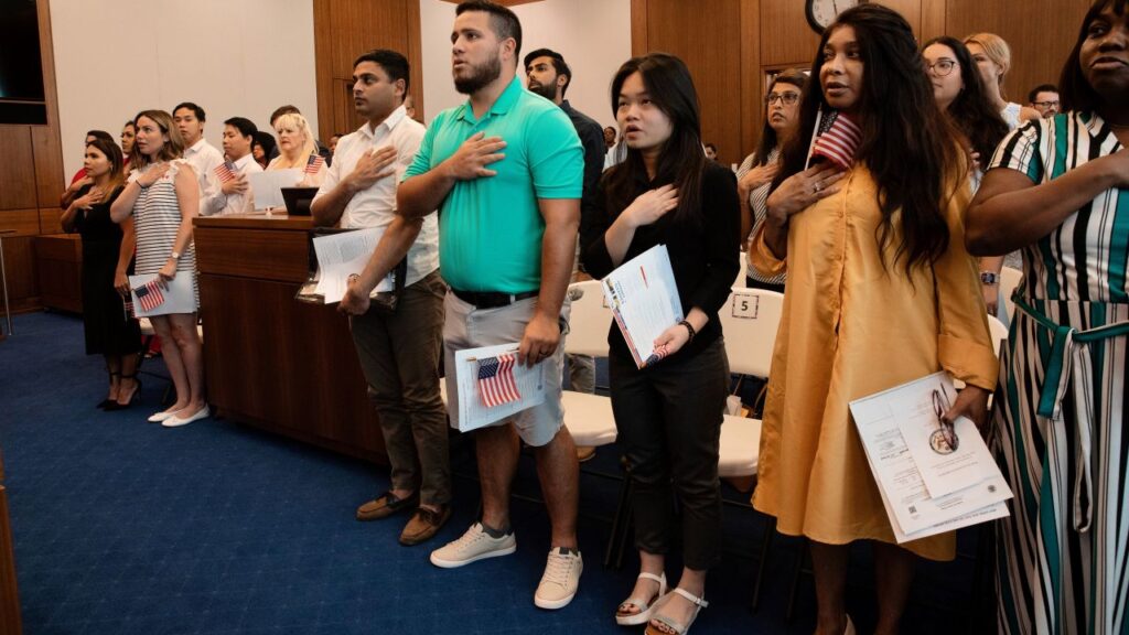 Image of immigrants reciting the Pledge of Allegiance during a naturalization ceremony in Savannah, Georgia. All are looking left and holding their hands over their hearts.