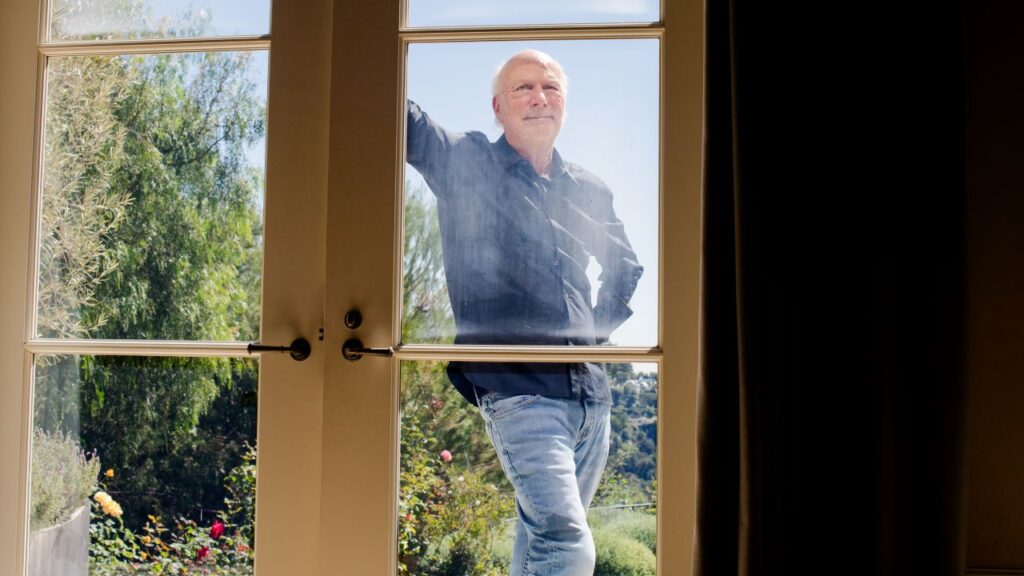Image of James Burrows in blue jeans and a blue shirt staring through French door windows