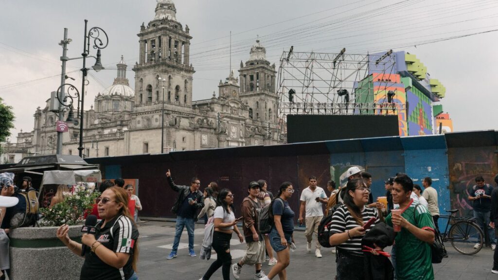 Tourists and locals pass by barricades erected to prevent disruptions from demonstrations at the Zocalo, Mexico City’s historic center square, on June 10, 2026, the day before the city was to host the World Cup opener. For many Mexicans, the World Cup is a chance to show the world that it is a thriving, cosmopolitan country. But for the protesters, it is a chance to show how far Mexico still has to go to provide security and equality for average citizens. (Luis Antonio Rojas/The New York Times)