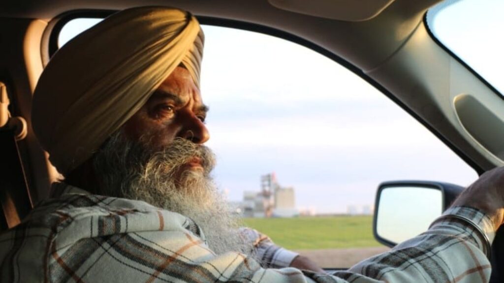 Image of a man in a checked shirt and head scarf facing right as he drives his truck