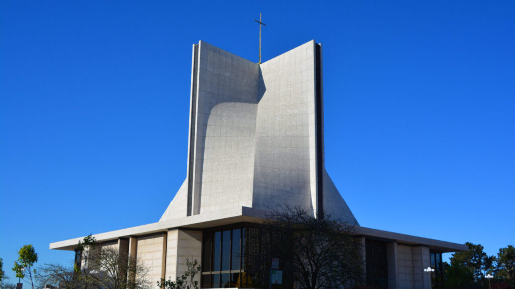 Image of a Catholic church with a modern exterior design. The church stands below a bright blue sky
