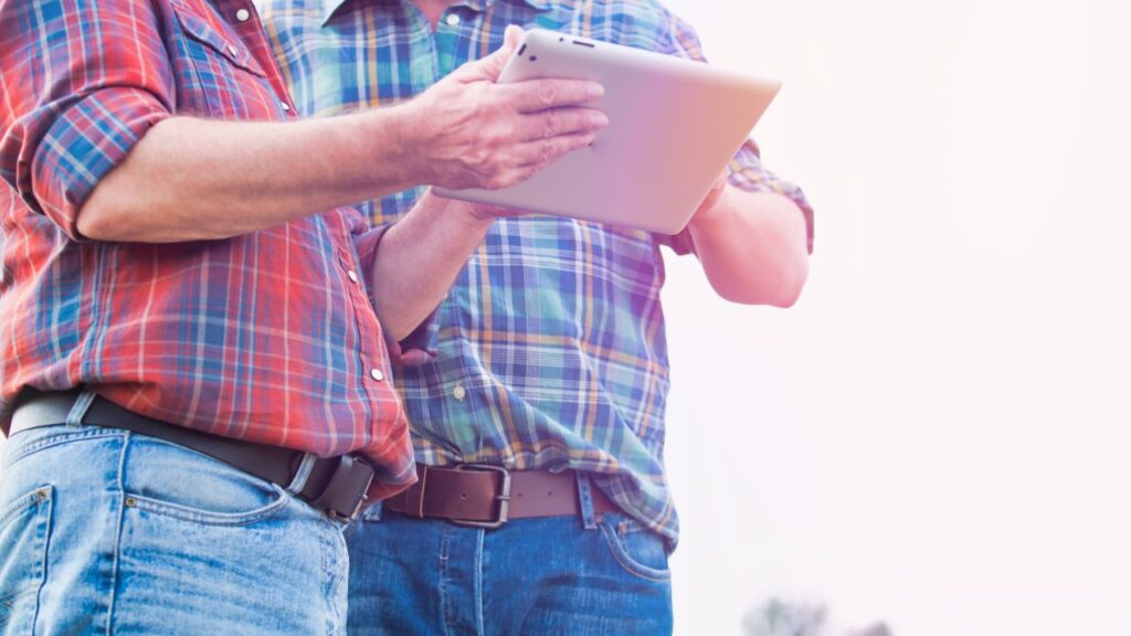 Image of two farmers in plaid shirts and blue jeans poring over data on a laptop