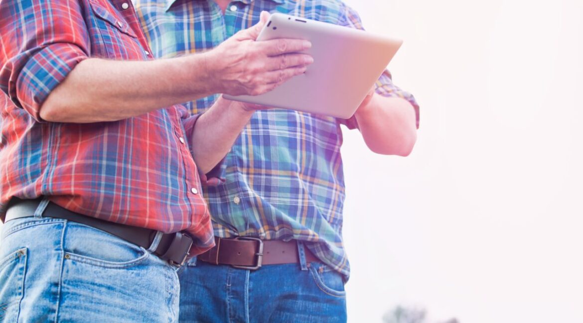 Image of two farmers in plaid shirts and blue jeans poring over data on a laptop