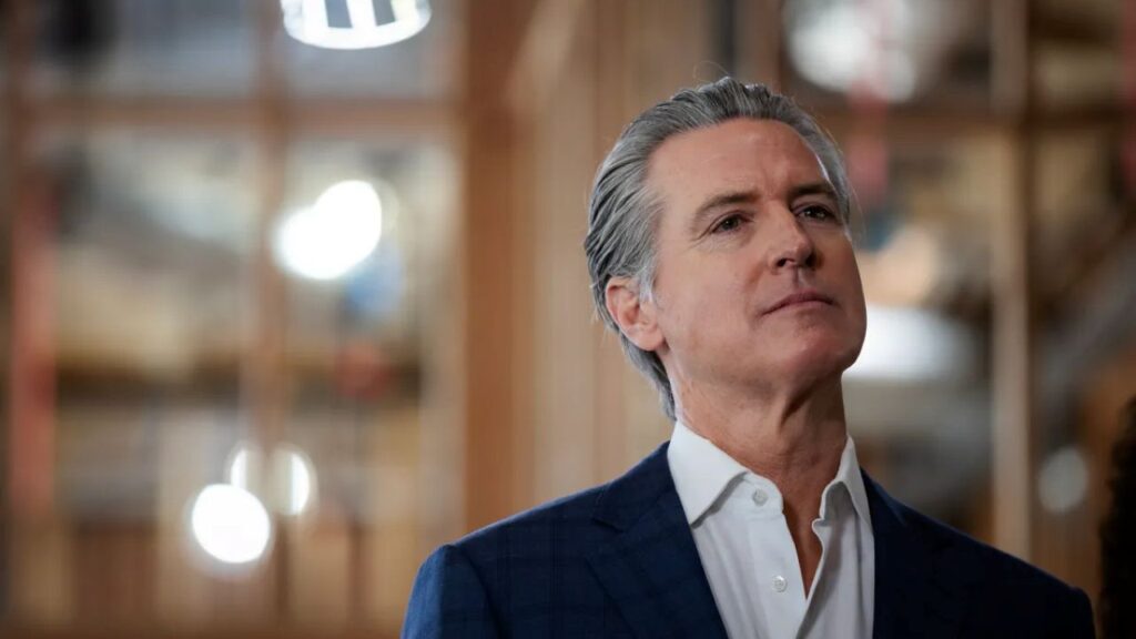 Image of Gavin Newsom in a blue suit and white open collar shirt looking up to the right