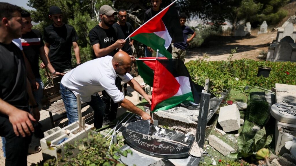 A Palestinian man places Palestinian flags on graves broken by Israeli soldiers near Nablus in the Israeli-occupied West Bank, July 31, 2026. REUTERS/Ammar Awad