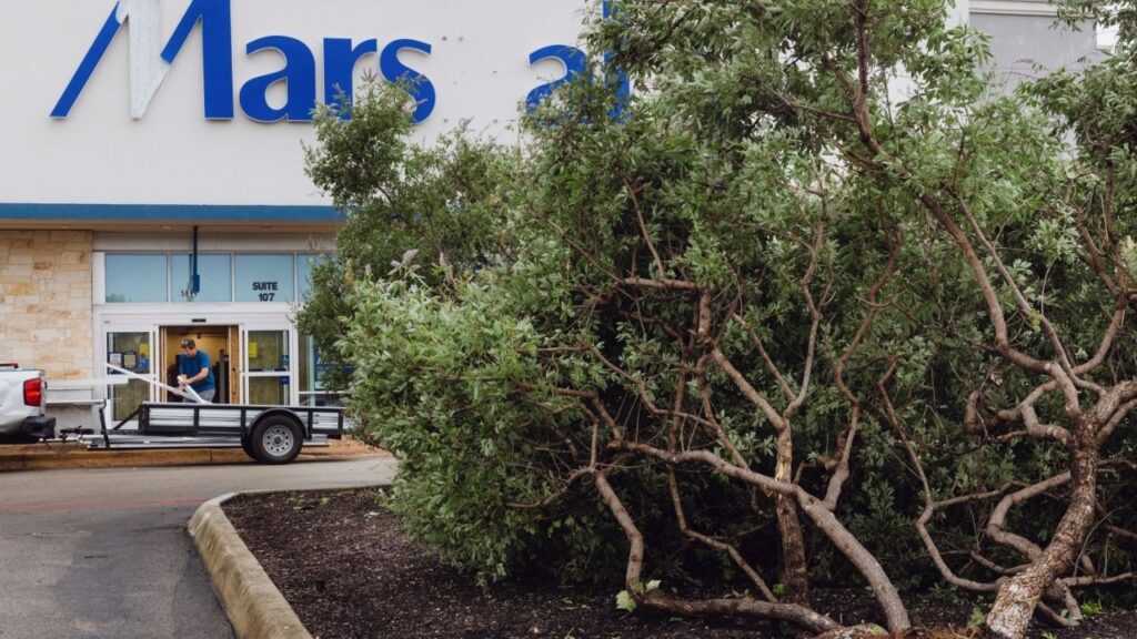 A fallen tree and damaged storefront after a tornado at a Marshall’s store in San Antonio, Texas, on Thursday, July 16, 2026. The tornado uprooted trees, battered the facade of the store and tossed air conditioners onto buildings. (Christopher Lee/The New York Times)