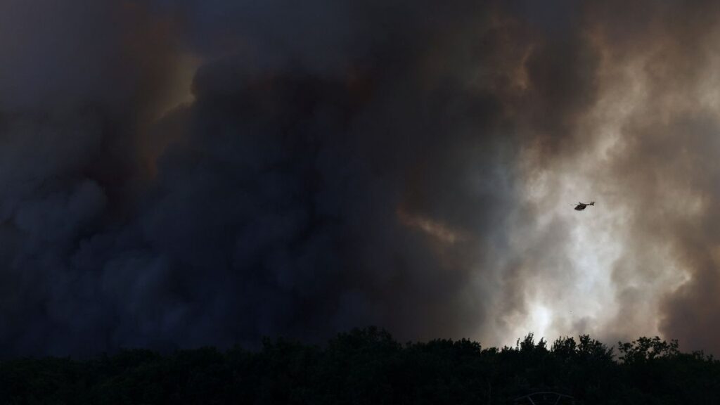 A firefighting helicopter flies through plumes of smoke above the Fontainebleau forest as a wildfire burns near Paris during a heatwave affecting large parts of France, July 13, 2026. (Reuters/Stephane Mahe)