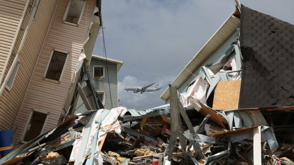 Debris lies on the street amid damaged buildings with an aircraft flying in the background, in the aftermath of the June 24 earthquakes, in La Guaira, Venezuela, July 6, 2026. (Reuters/Ricardo Arduengo)