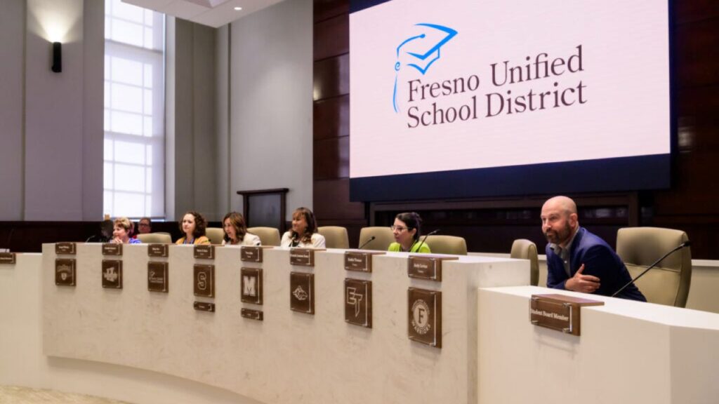 Sweeping view of Fresno Unified trustees at the dais in front of a screen with the Fresno Unified logo and the words "Fresno Unified School District"
