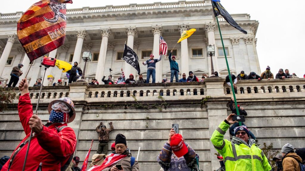 Image of rioters standing in front of and on the U.S. Capitol with flags raised