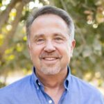 Portrait of Jim Zion in a blue open collar shirt in a pistachio orchard