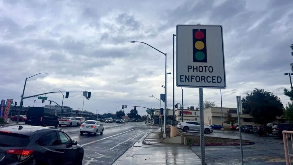 Image of a sign warning of red light camera enforcement on a rainy busy Merced street