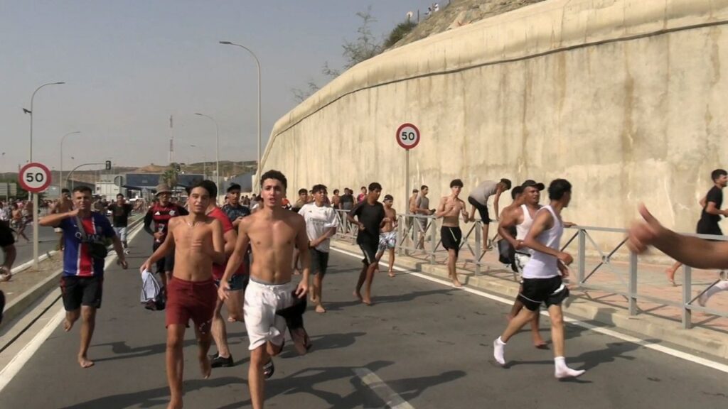 Migrants run and cheer as they cross on foot into the North African enclave of Ceuta from Morocco, after swimming over from the Moroccan side and overwhelming police at the city's breakwater, according to Spain's Guardia Civil, in Ceuta, Spain, July 30, 2026, in this screengrab obtained from a handout video. FARO TV via REUTERS