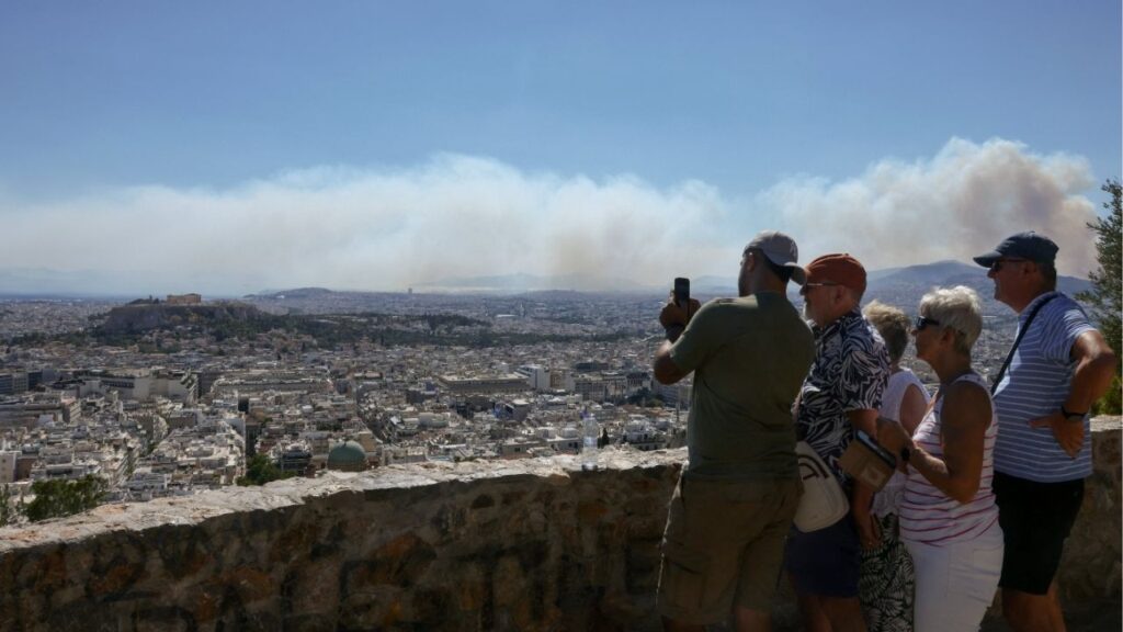 People take photos of the view with the Parthenon temple atop the Acropolis hill, as smoke from a wildfire burning near Haidari blankets Athens, Greece, July 31, 2026. (Reuters/Louiza Vradi)