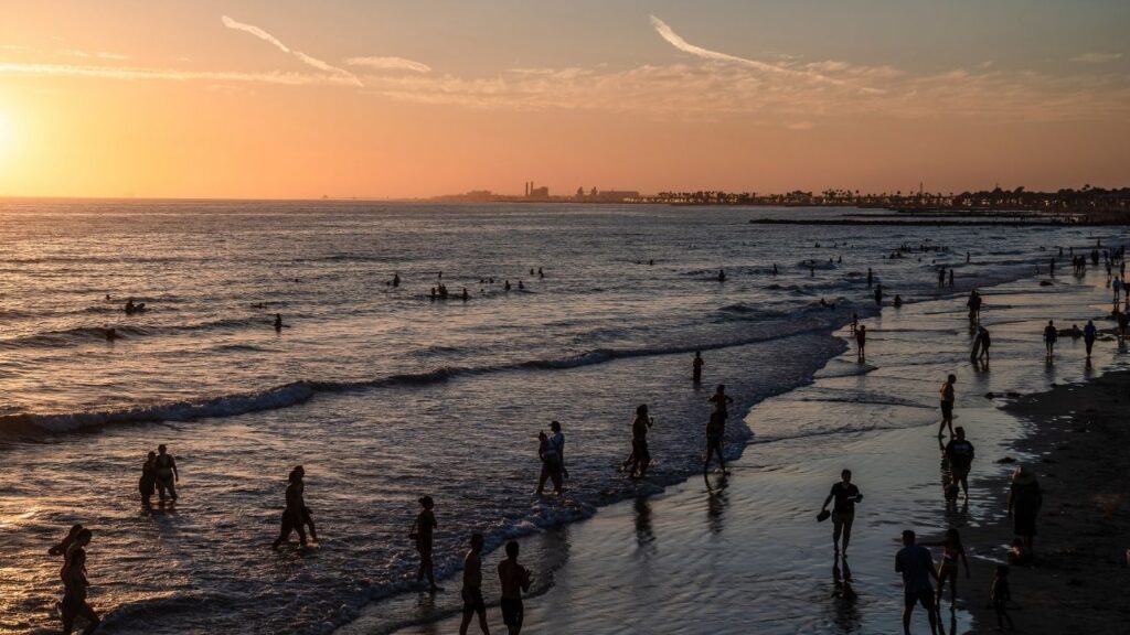 The sun sets over visitors in the water at Newport Beach, Calif., July 15, 2026. More than 400 people were arrested in the city on the July 4 weekend after a social media “takeover” got out of hand. Now the city is trying to figure out how to stop it from happening again. (Ariana Drehsler/The New York Times)