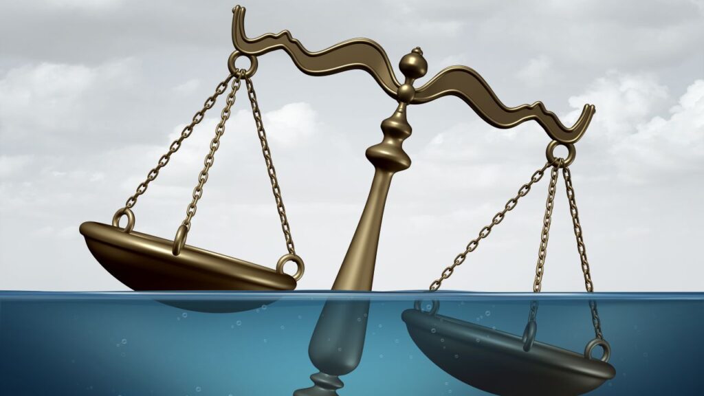 Composite image of bronze scales of justice partially submerged into blue water symbolizing a court battle over water rights