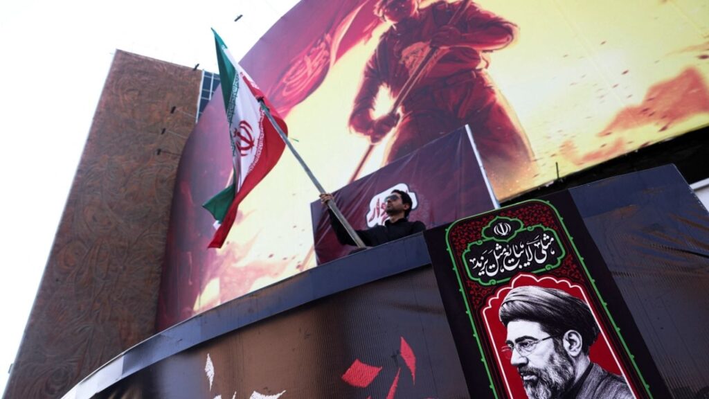 A man holds an Iranian flag, next to a picture of Iran's Supreme Leader Mojtaba Khamenei, in Tehran, Iran, August 13, 2026. (Reuters File)