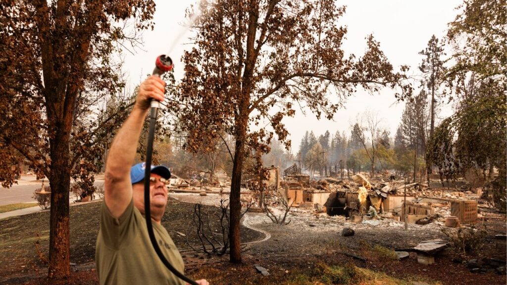 A member of the Seaton family hoses down their yard after the Old Trail fire leveled homes in their neighborhood in Spokane, Wash., on Sunday, Aug. 2, 2026. Hundreds of structures were destroyed and thousands of people in Spokane County, Wash., remained under evacuation orders on Sunday as firefighters continued their efforts to knock back and control several blazes in the area. (John Stember/The New York Times)