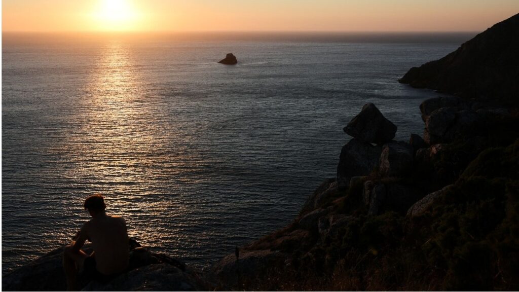 A tourist looks at the sunset the day before the solar eclipse, on the Costa da Morte ("Coast of Death"), once considered the end of the world and a traditional destination for pilgrims completing the Camino de Santiago, in northwestern Spain, August 11, 2026. REUTERS/Nacho Doce