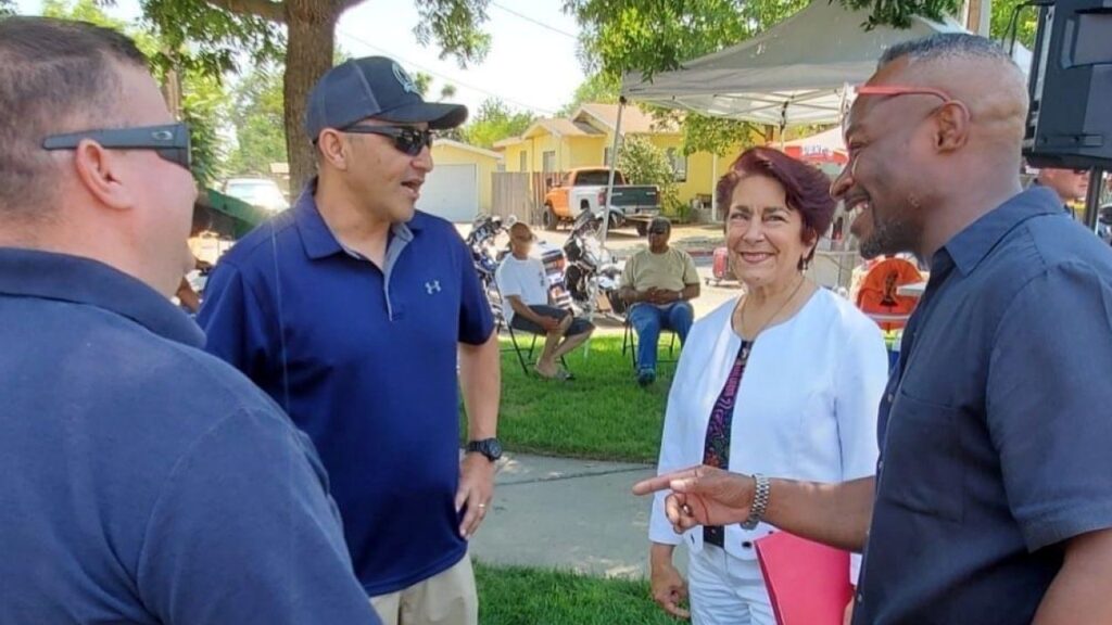 State Sen. Anna Caballero in a white jacket and pants talking with three men in blue shirts at an event