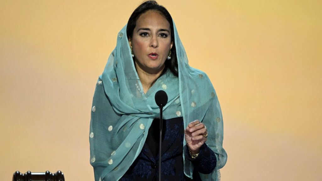 Image of Harmeet Dhillon in traditional Sikh clothing against a yellow backdrop speaking on stage
