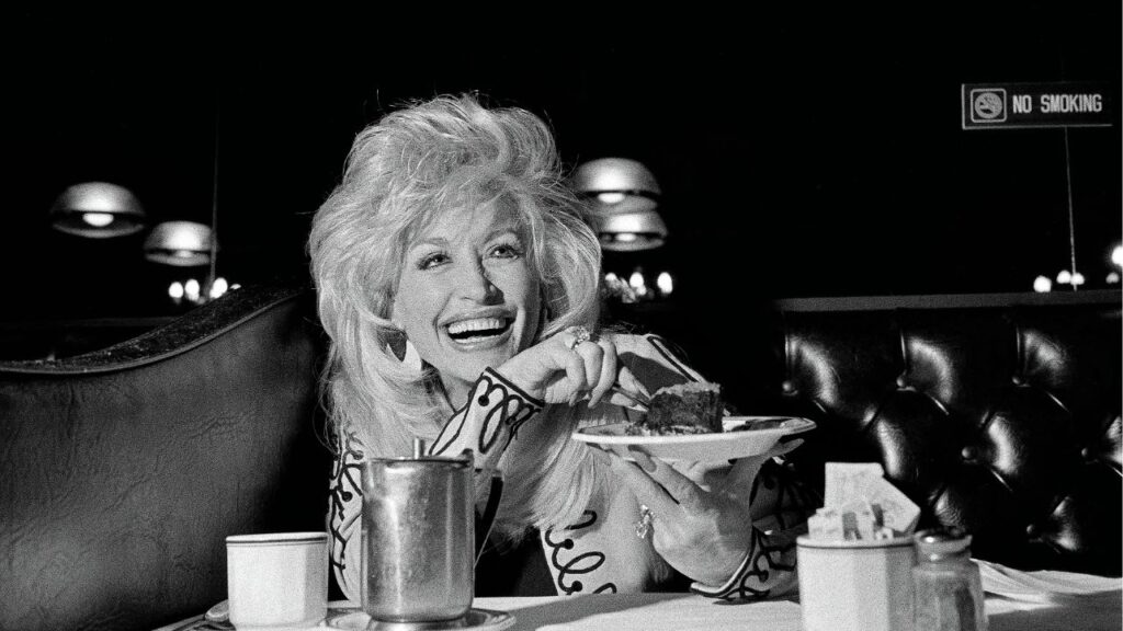 Dolly Parton savoring a chocolate mousse cake in New York in 1992. The top-selling singer, songwriter, and entrepreneur died at 80 on Tuesday, Aug. 25, 2026. With her bedazzled, bewigged, and bodacious style, she used her clothes and her body to subvert expectations. (Edward Keating/The New York Times)