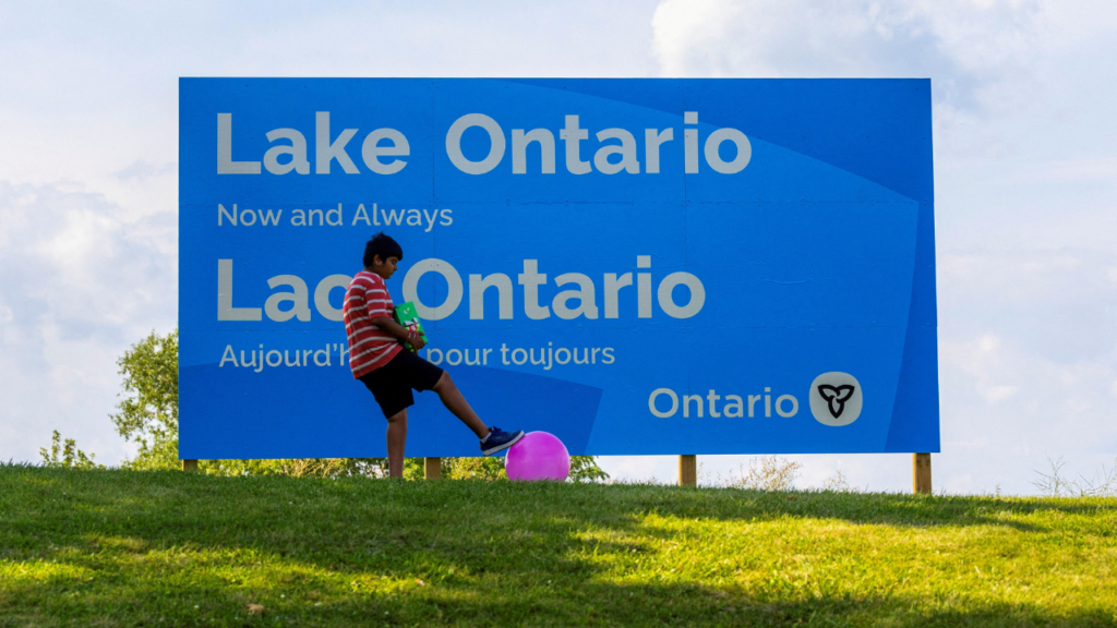A young child plays with a ball near a sign reading "Lake Ontario, Now and Always," unveiled by Ontario Premier Doug Ford at Fifty Point Conservation Area, after U.S. President Donald Trump signed an executive order renaming Lake Ontario as "Lake America," near Grimsby, Ontario, Canada, August 29, 2026. (REUTERS/Carlos Osorio)
