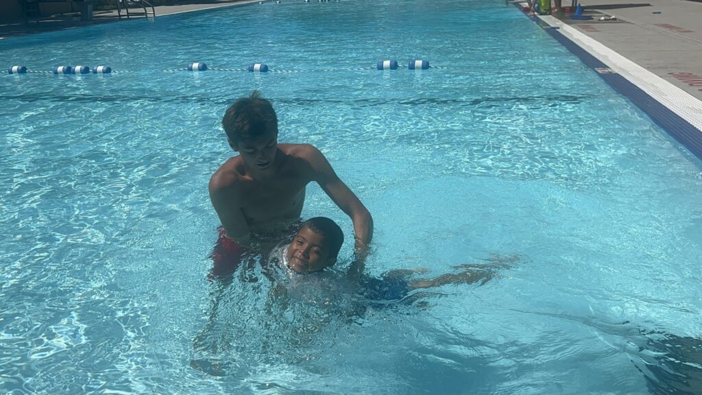 Image of a young boy learning swim while being held by an instructor in a pool