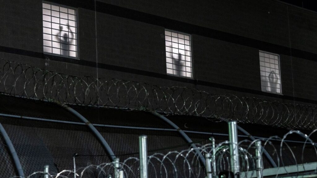 Inmates stands at windows at the Delaney Hall immigration detention center in Newark, N.J., as demonstrators gather outside, May 28, 2026. The deaths of three Immigration and Customs Enforcement detainees in less than eight months have raised urgent questions about the medical services provided at Delaney Hall and at other detention centers, with immigrants and local officials describing haphazard health care. (Todd Heisler/The New York Times)