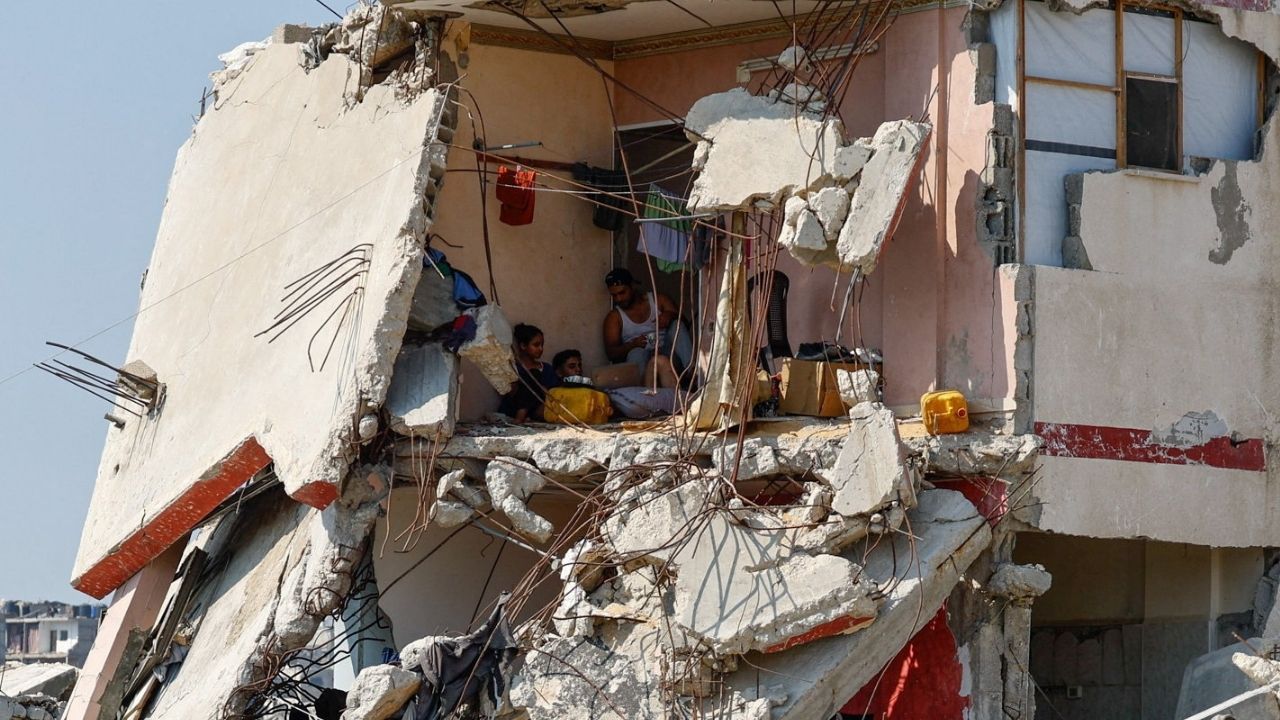 Palestinians sit inside a house damaged during the war, surrounded by destroyed buildings, in Gaza City, August 15, 2026. (Reuters/Mahmoud Issa)