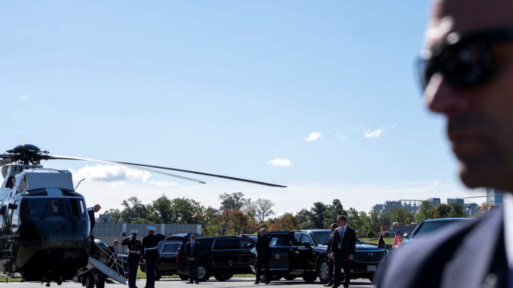 Image of a Secret Service agent in a blue suit wearing sunglasses facing left as President Trump's helicopter lands