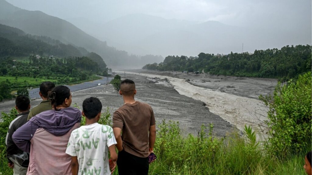 People look at a swollen river in the Devighat area of the Nuwakot district in Nepal on Friday, Aug. 28, 2026, in the aftermath of a devastating flash flood. Authorities in Nepal warned that more water from new lakes created by the landslide that triggered Wednesday’s flood could overflow and send more water rushing into the valleys. (Atul Loke/The New York Times)