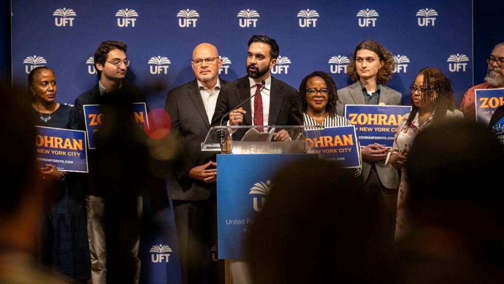 Zohran Mamdani, the Democratic nominee for New York City mayor, at an event in Manhattan, July 9, 2025. Mamdani is taking legal action against a bill championed by Michael Mulgrew, the president of the United Federation of Teachers, standing to the mayor’s right. (Dave Sanders/The New York Times)